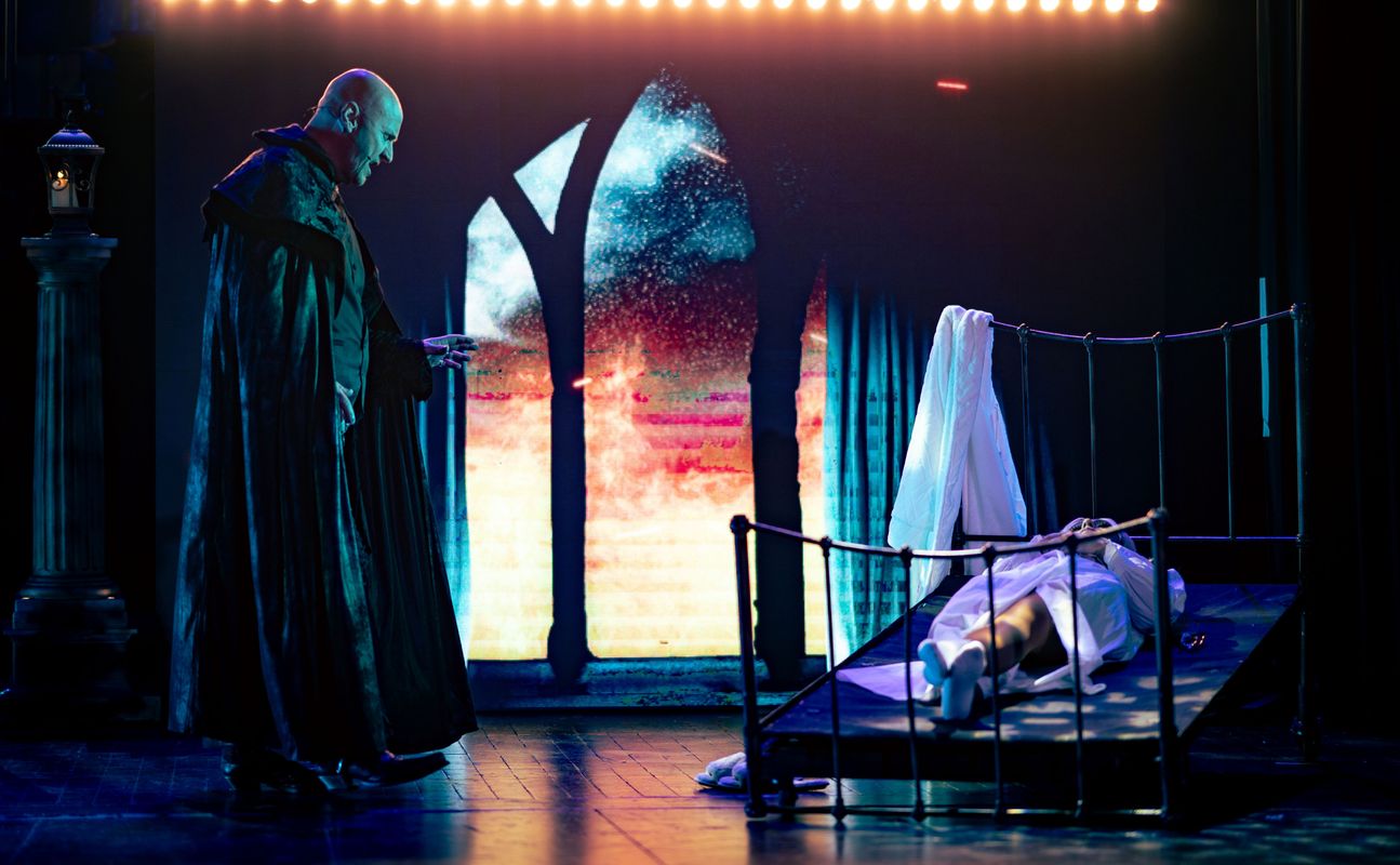 A dark figure looks over someone lying on a bed frame.