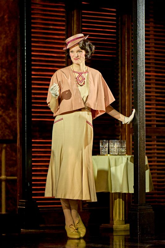 A person dressed in a pink jacket and cream dress outstretches their arm.