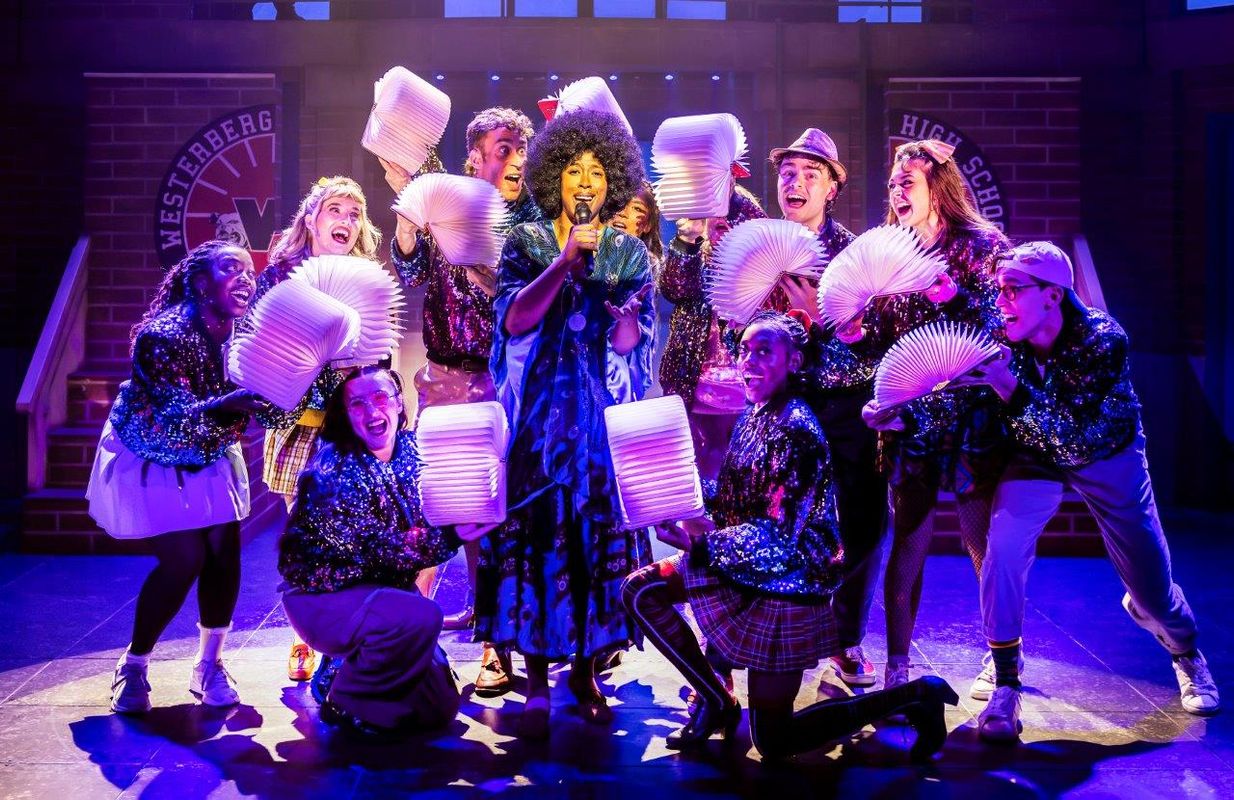A woman is stood in the middle of a group of people holding light up books whilst she is singing