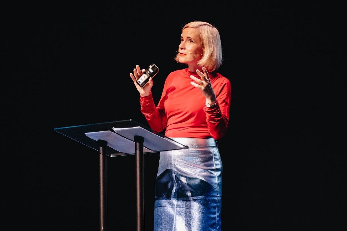 Lucy Worsley talking on stage. She is wearing a red top and a silver pencil skirt.