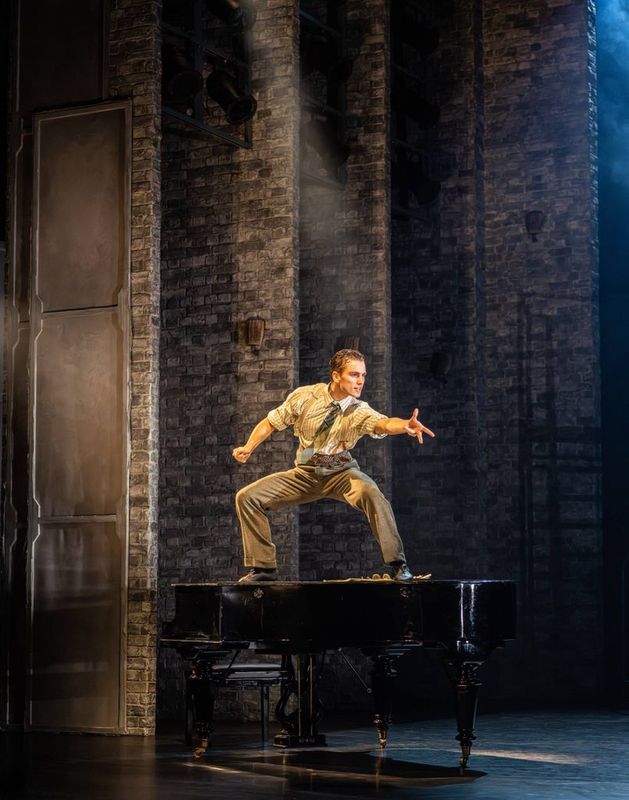 A person stands widely on a black grand piano.