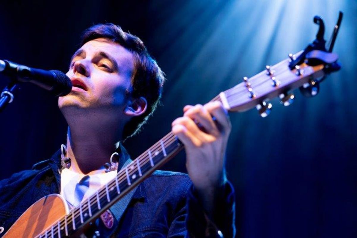 A man singing on stage into a microphone and playing an acoustic guitar