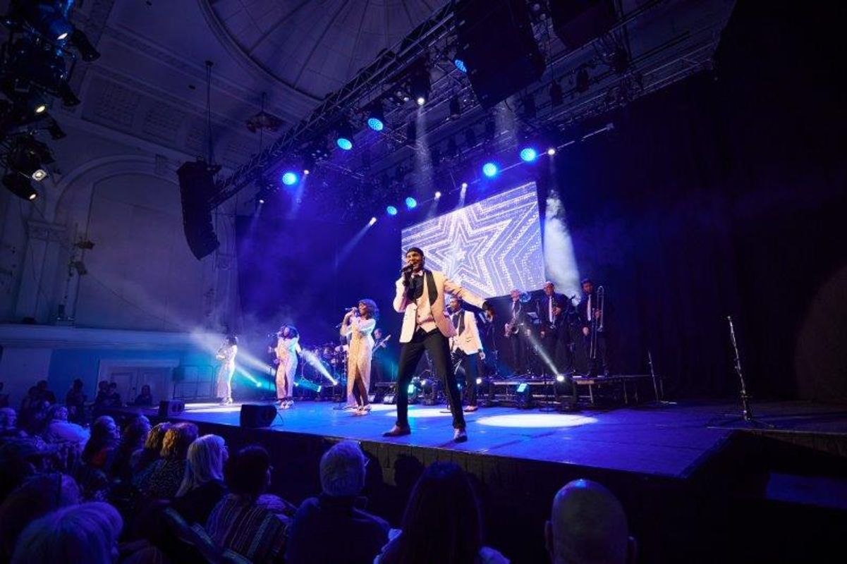 Three people are stood to the back of the stage with another person stood to the  front.