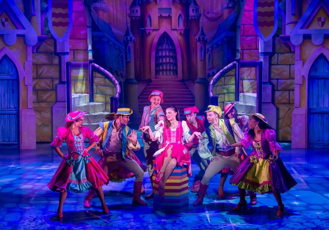 Cinderella sits down in a pink dress surrounded by ensemble members.