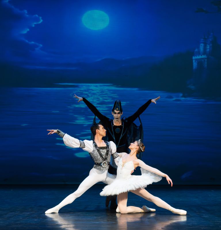 Three ballet dancers are positioned centre stage with one dressed all in black at the rear.