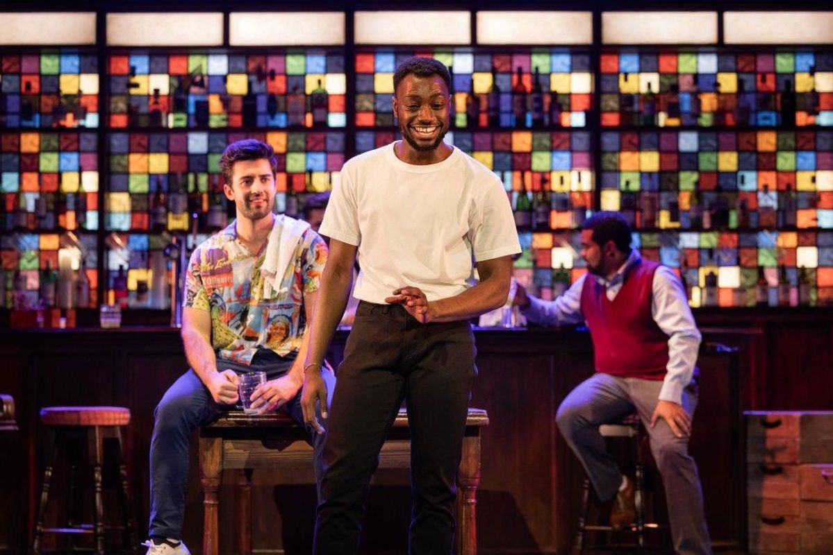 There is a person stood in the middle, two people behind them sat at the bar