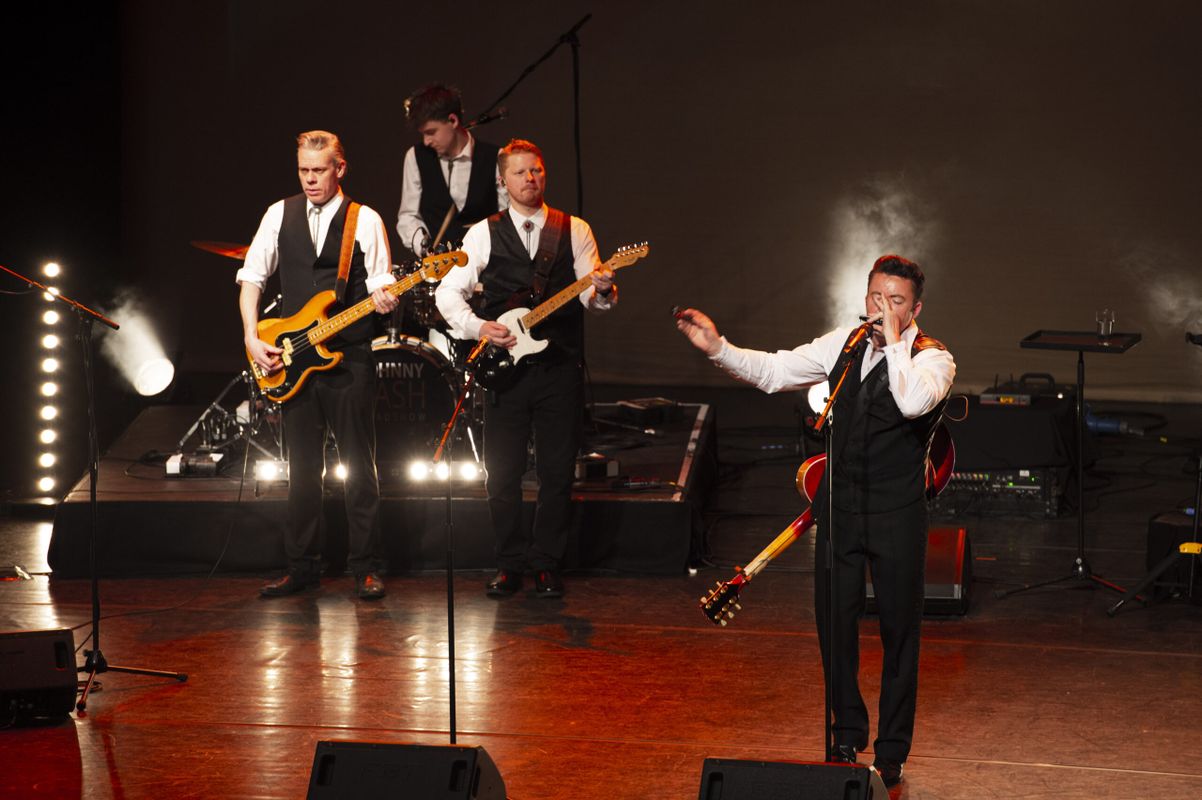 Three people dressed in black waistcoats play guitar and sing on stage.