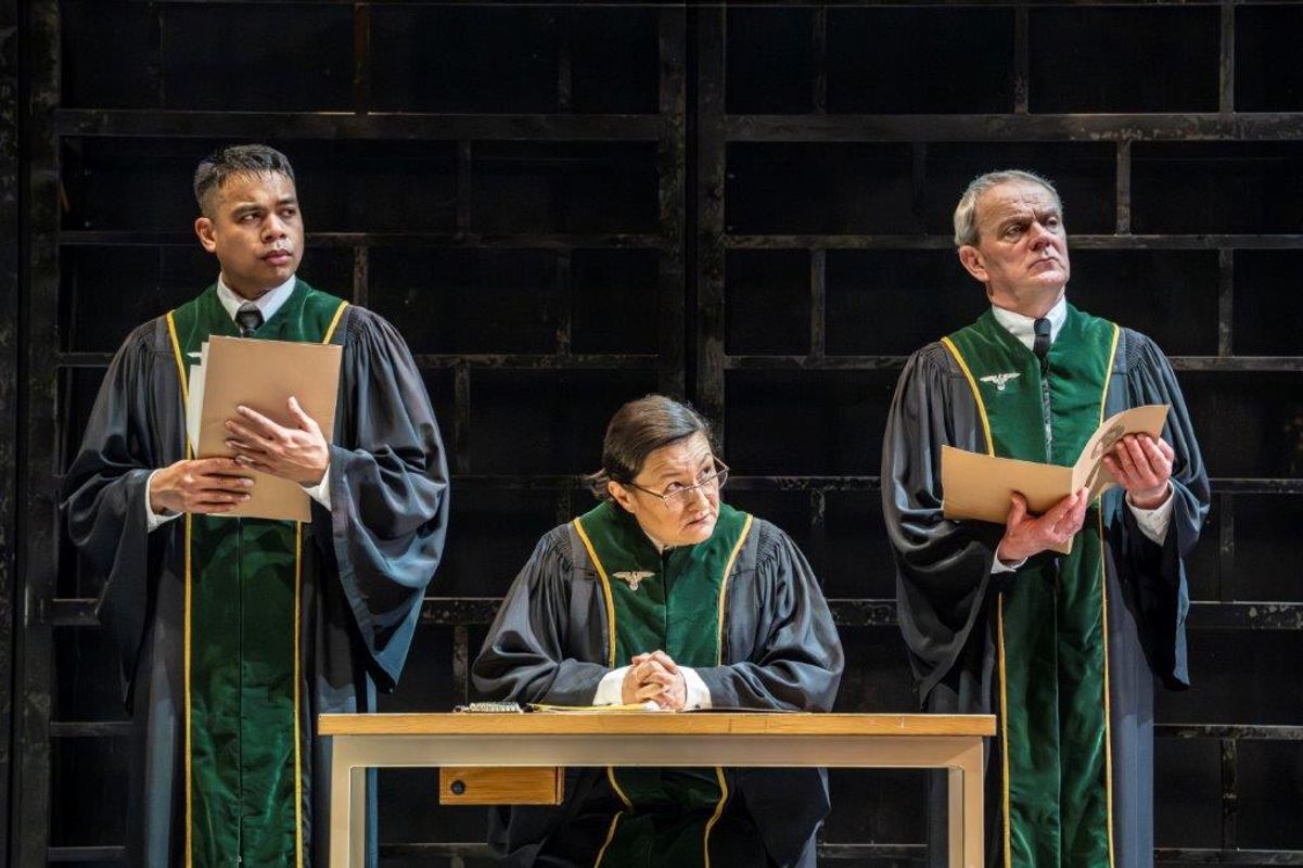 Three people wearing robes, one is sat at a table and the other two are stood either side