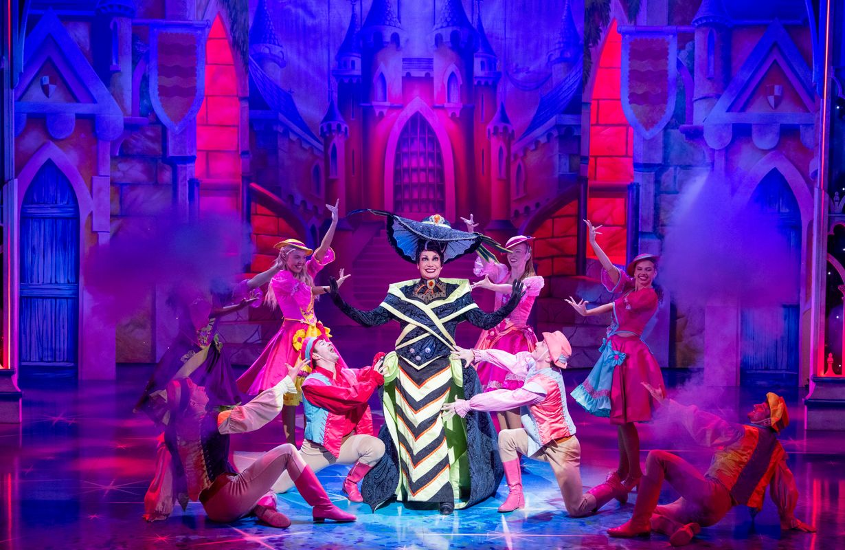 The Wicked Stepmother stands centre stage in a black and yellow dress with a floppy hat.