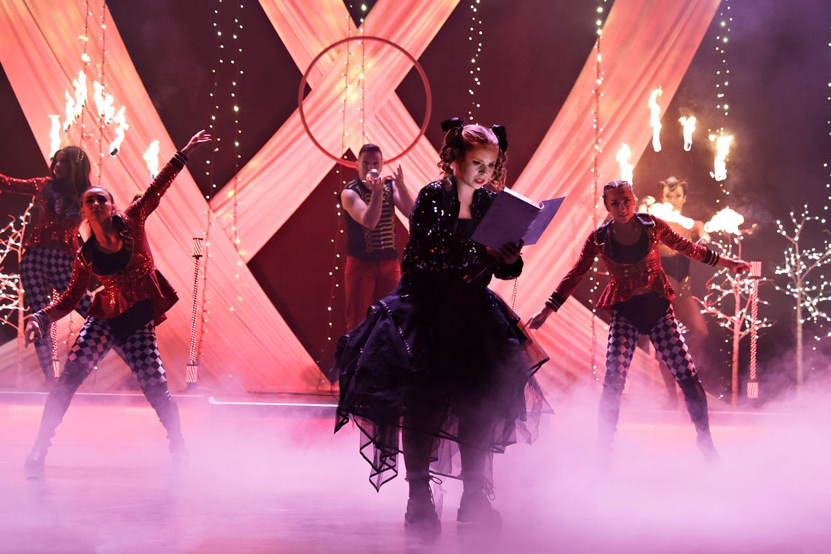 A person dressed in a black skirt and sequined jacket reads a book.