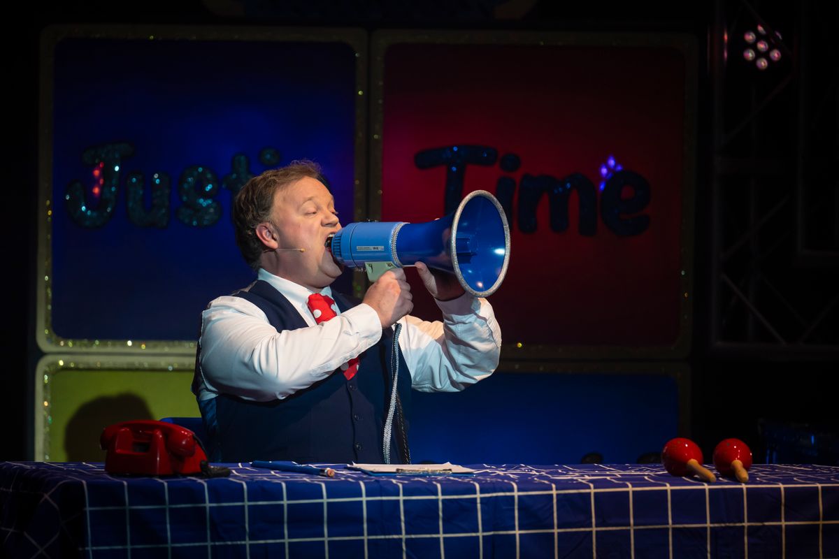 Justin dressed in a waistcoat uses a megaphone.