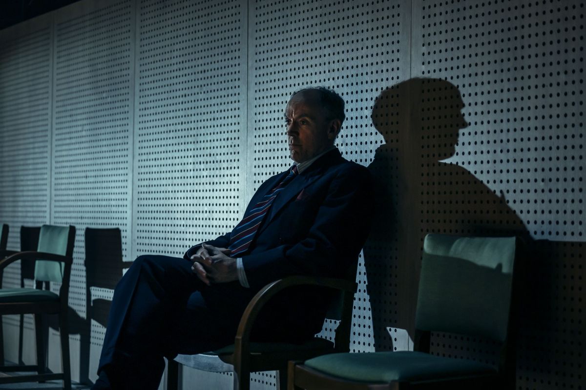 A person sits on a chair with their shadow projecting on the background.