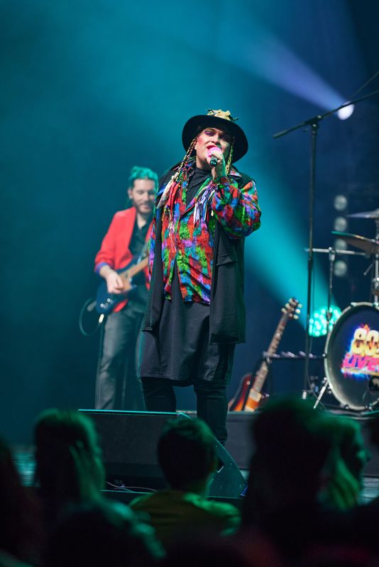 A person wearing a rainbow coloured shirt sings on stage.