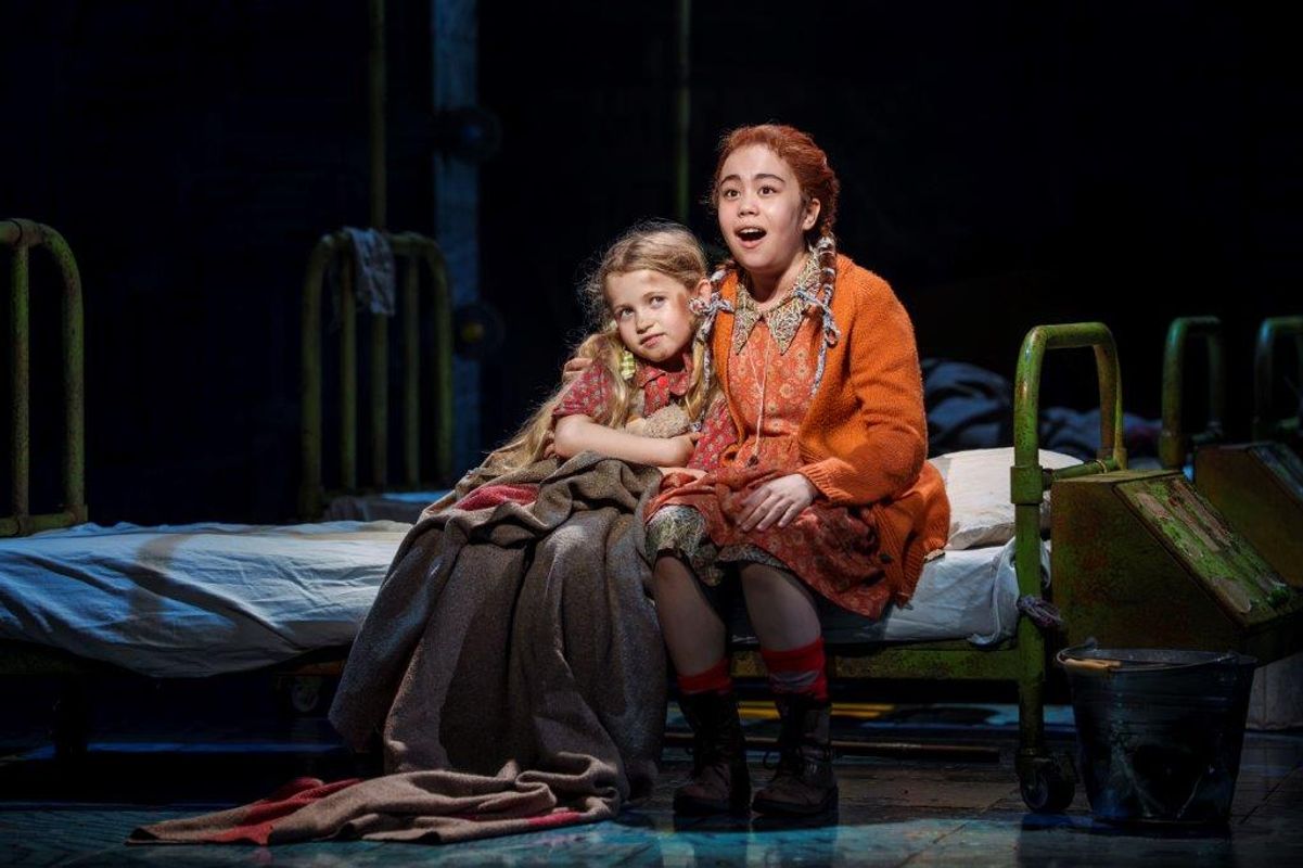 There are two young girls sitting on a bed, they are wearing tatty clothes