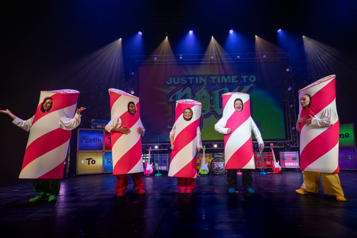 Five cast members stand on stage in red and white striped tube costumes.