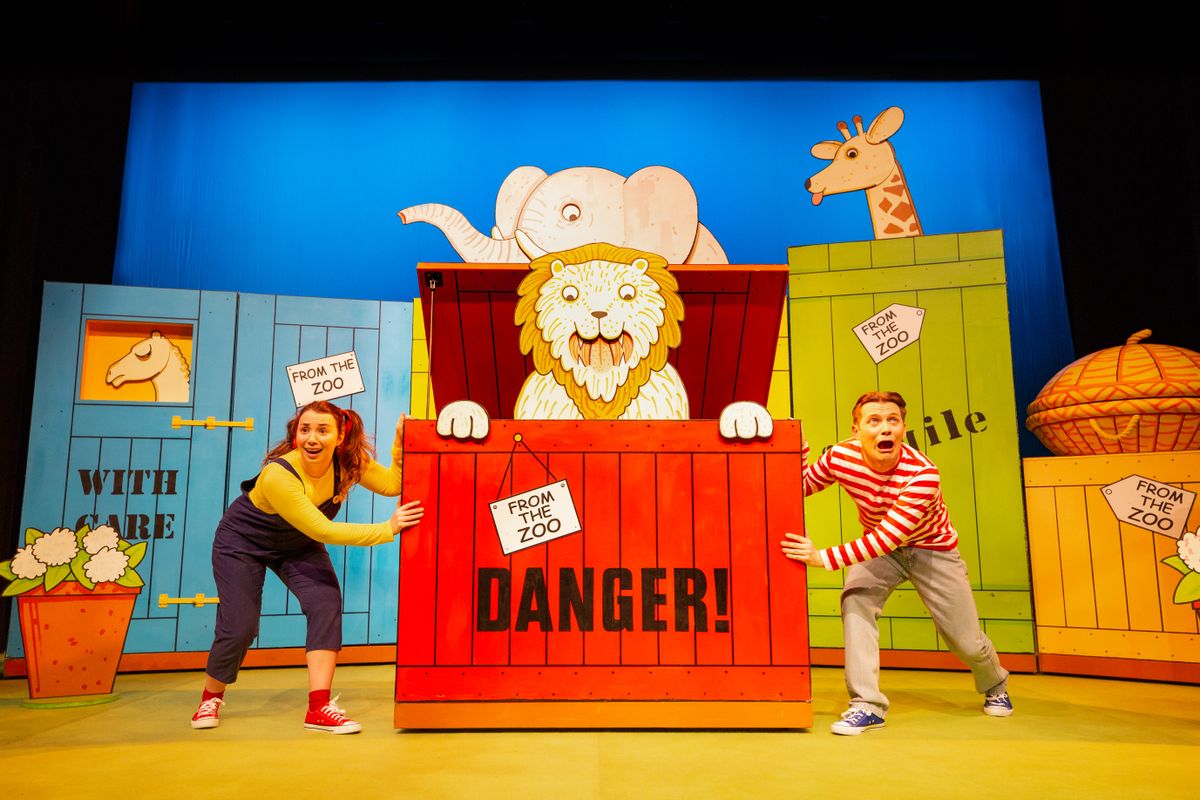 There is a giant red crate, with the word DANGER on it, a cartoon lion poking out the top. There are two people stood either side of the crate kneeling down.