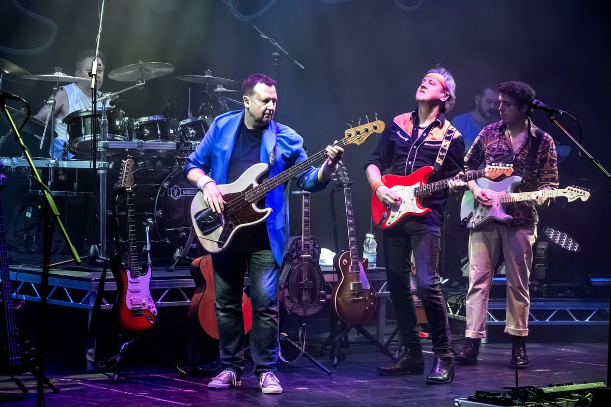 Band on stage performing, they're playing guitars and drums and there are flashing lights around them