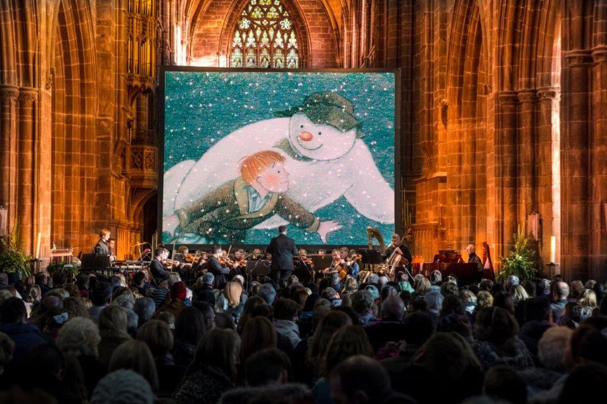 People performing on stage with The Snowman on a projector behind them.