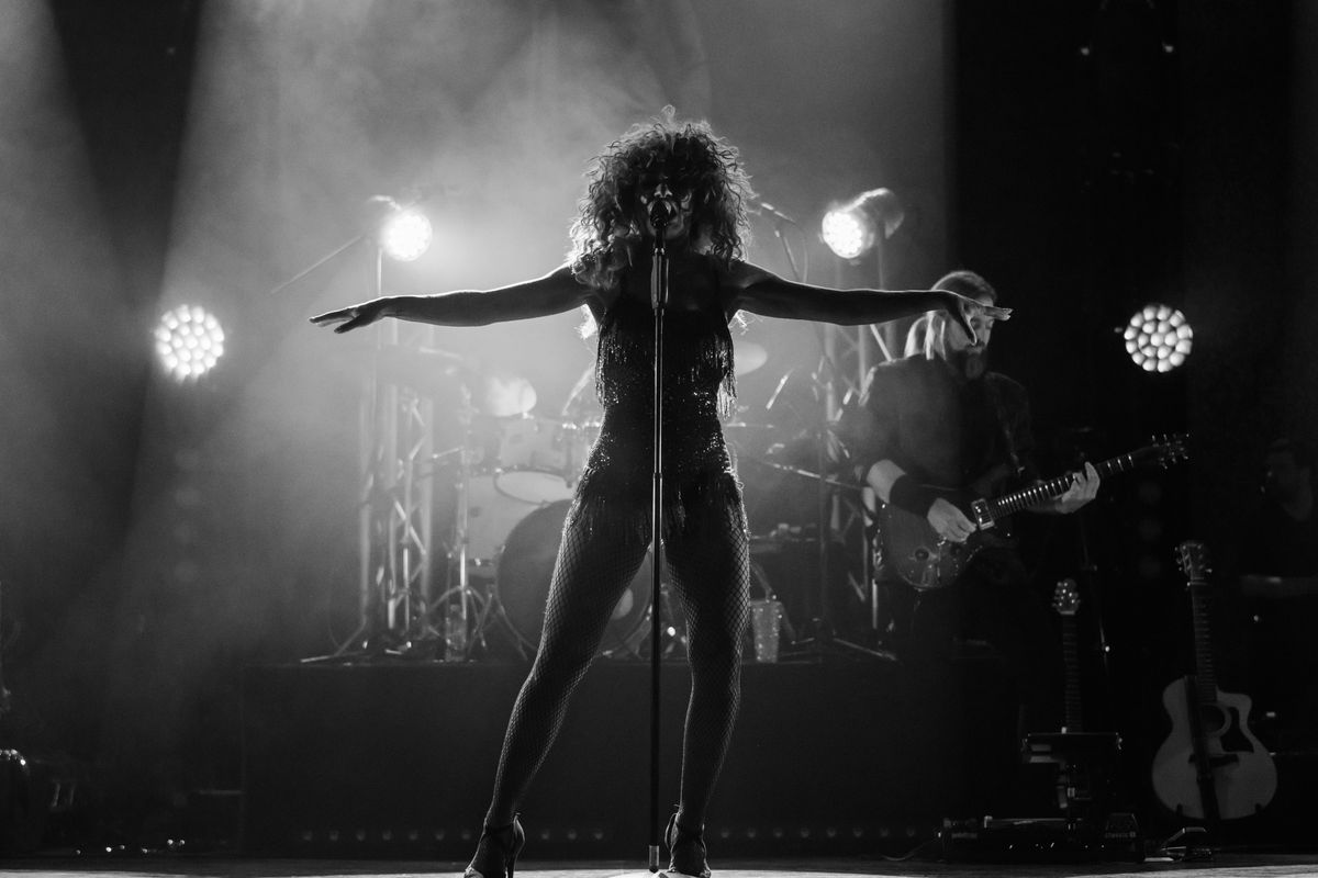 A person lit by a spotlight stands with both arms out to the side.