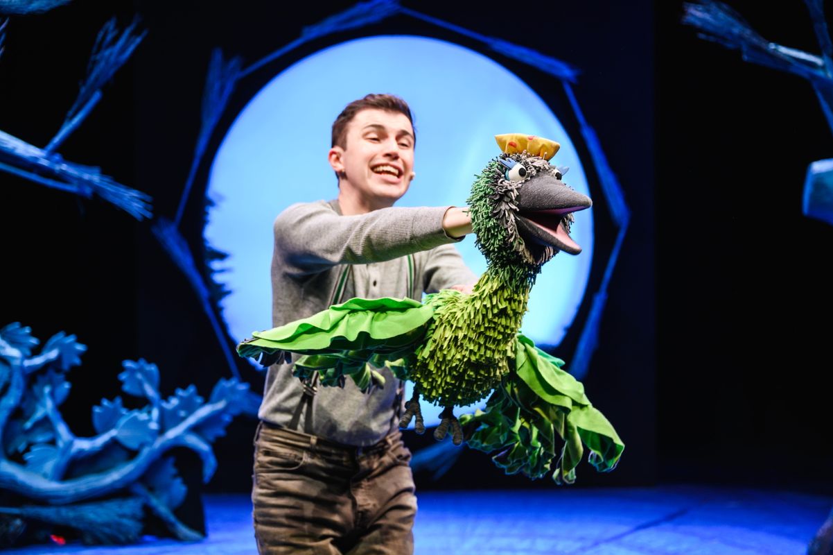 Actor holding a bird puppet on stage.