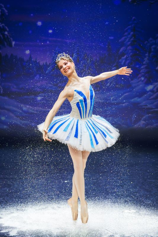 A ballet dancer dances on stage dressed in a white tutu with blue and silver stripes.