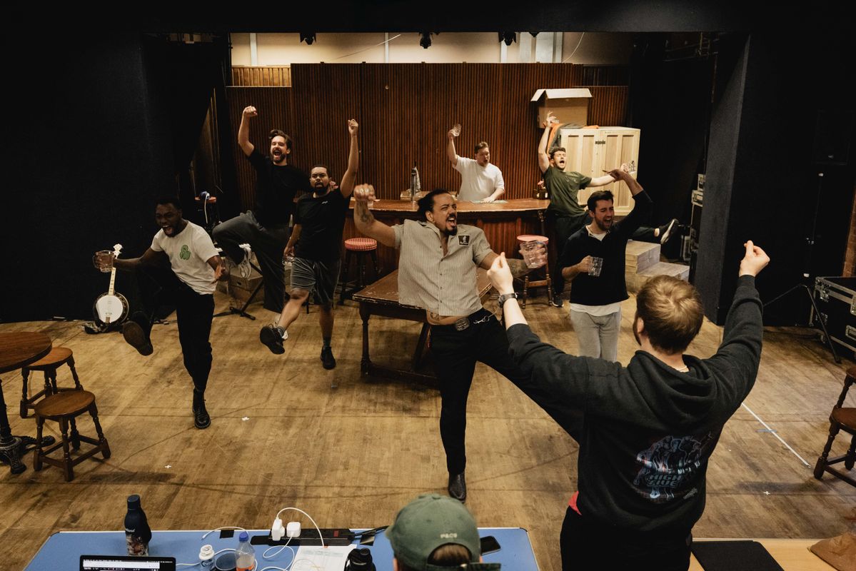 Group on men in a pub like setting, dancing and singing