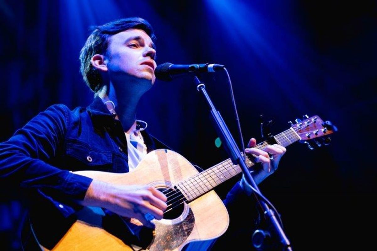 A man singing on stage into a microphone and playing an acoustic guitar
