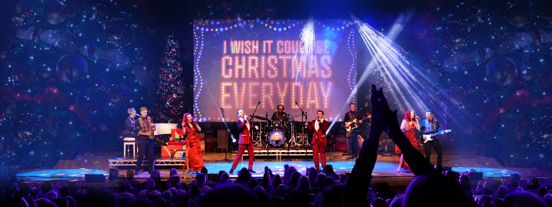 Four people in red outfits are singing on stage with the band in the background.