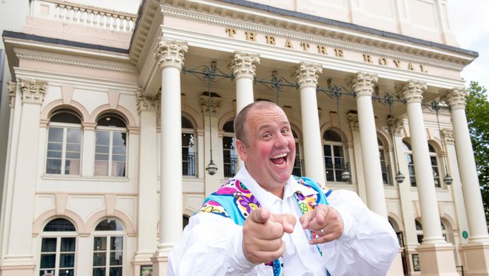 An actor playing the sidekick cheekily smiles and points at the camera.