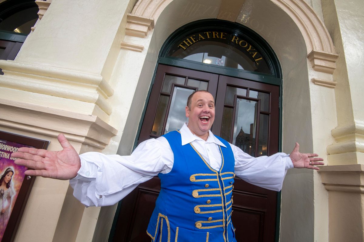 Buttons stand outside the Theatre Royal entrance with his arms out to the side.