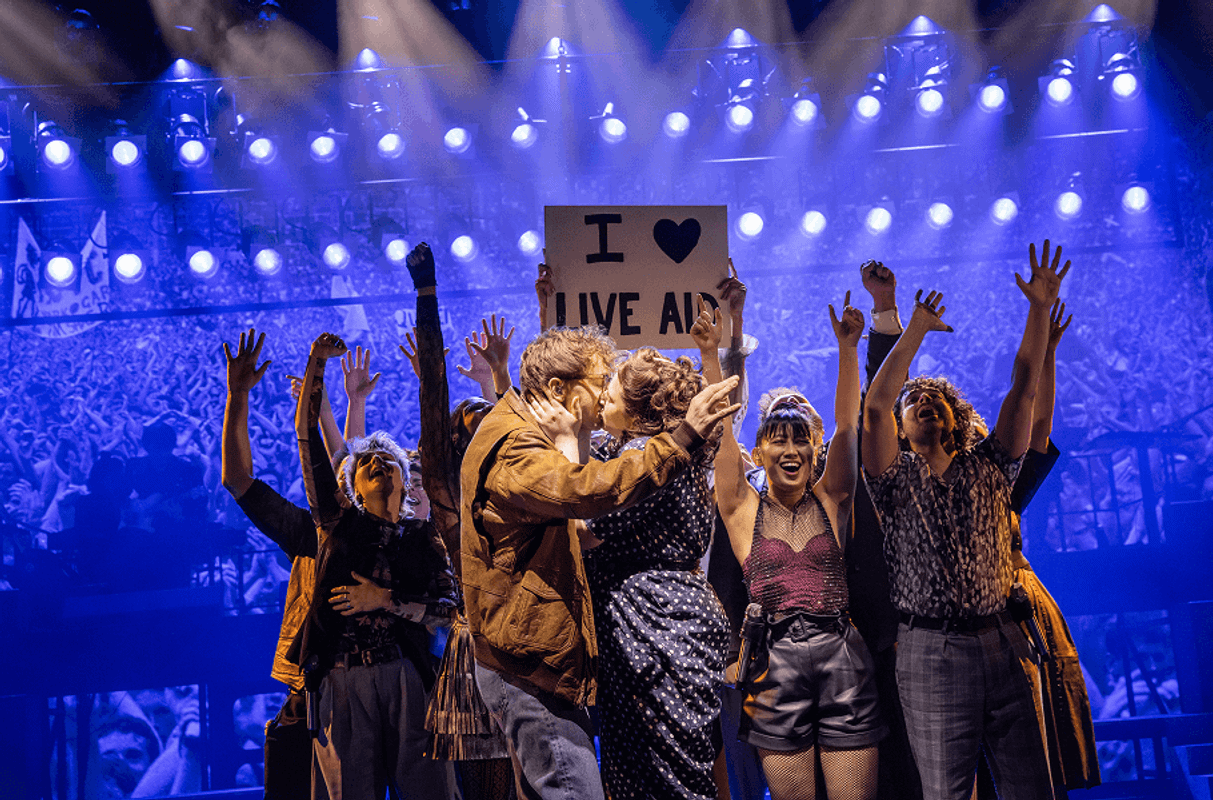 Two people kissing with people behind them cheering