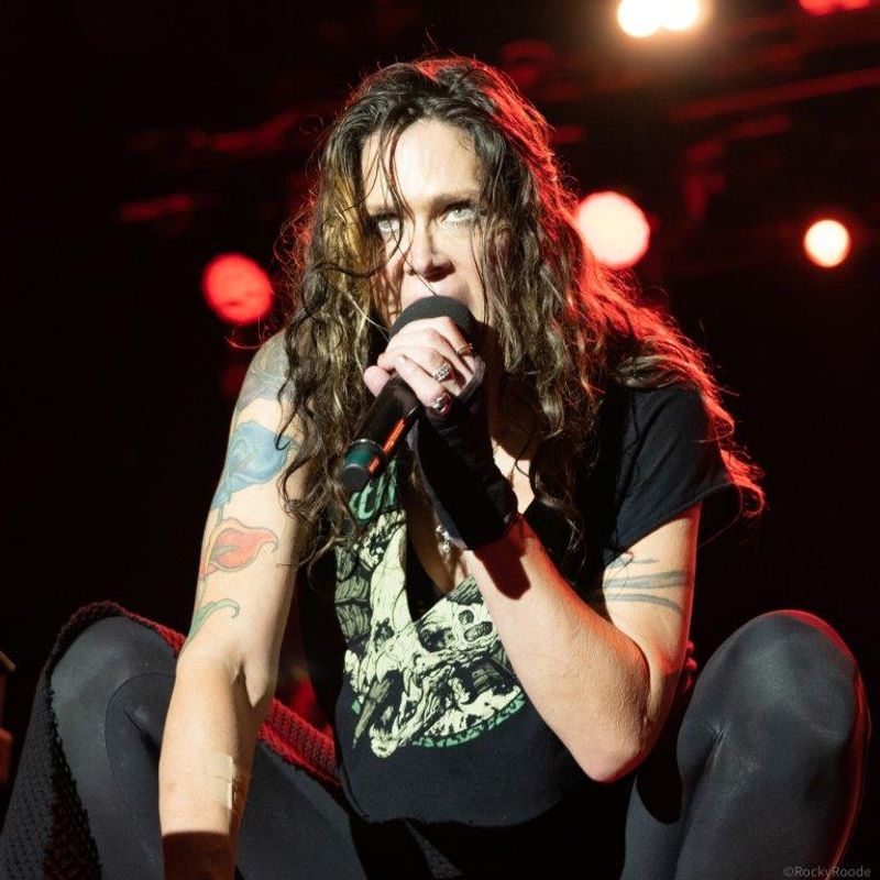 A person with a tattoo on their right arm crouches down whilst singing.