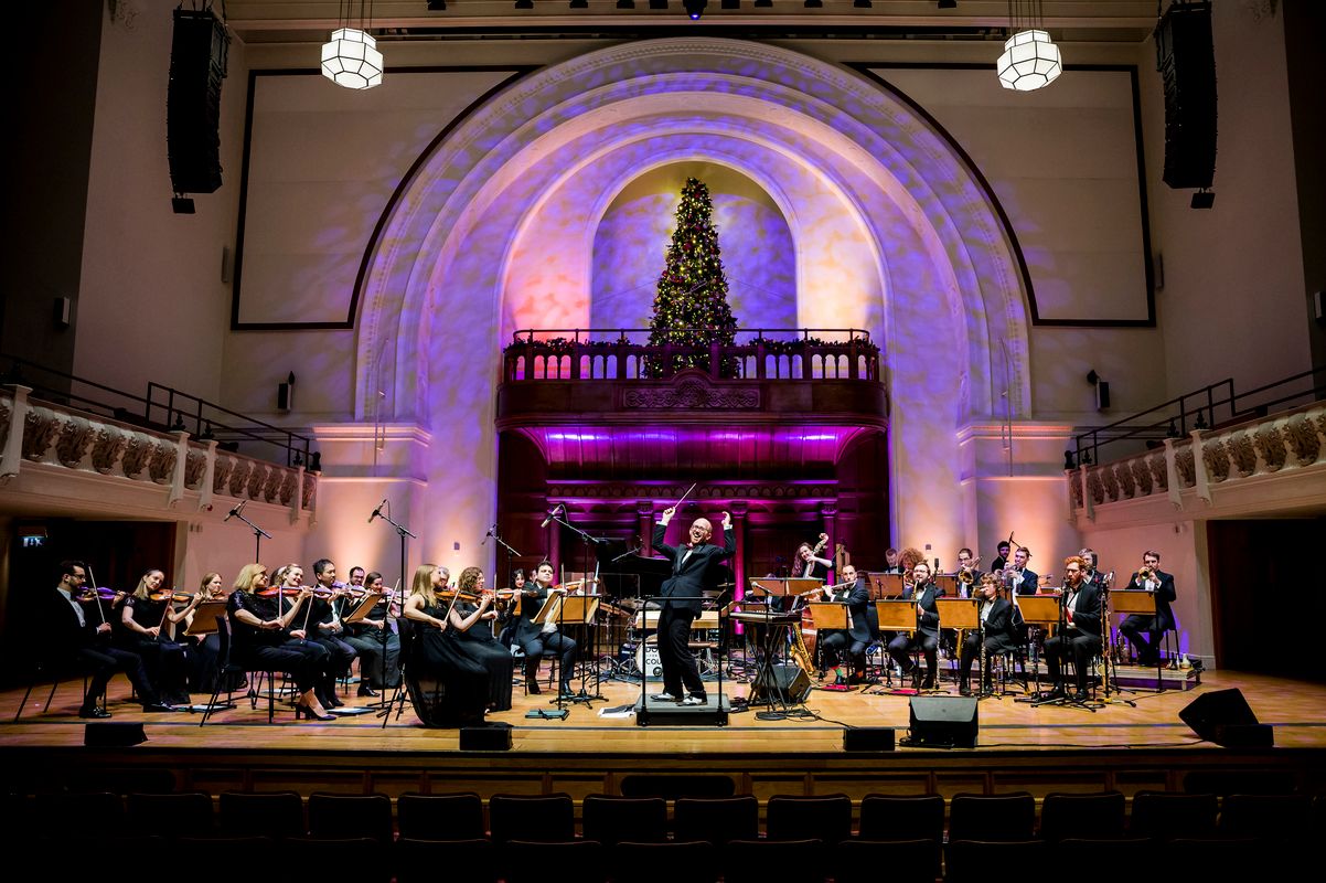 The orchestra play with the conductor joyfully gesturing to the audience.