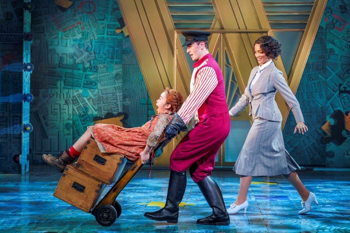 A gentleman is pushing a young girl around on wooden boxes that are being wheeled about on a dolly