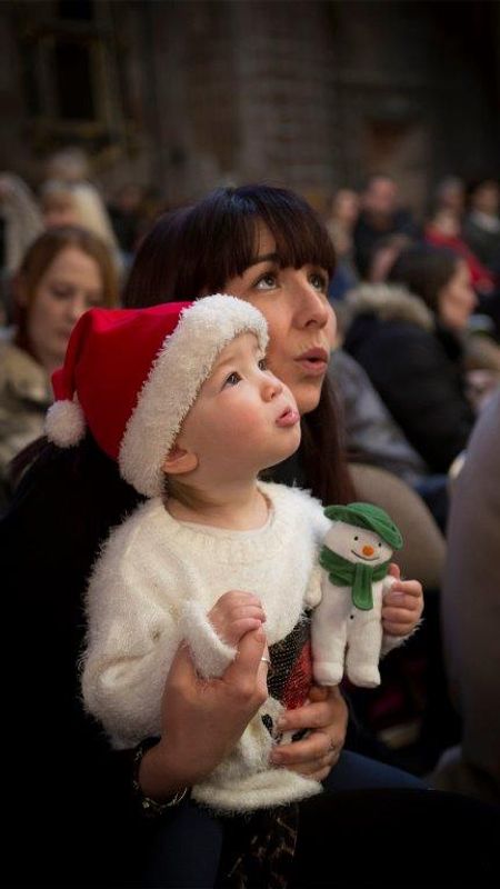 A mum and baby watching the performance. The baby is holding a plushie snowman and wearing a santa hat