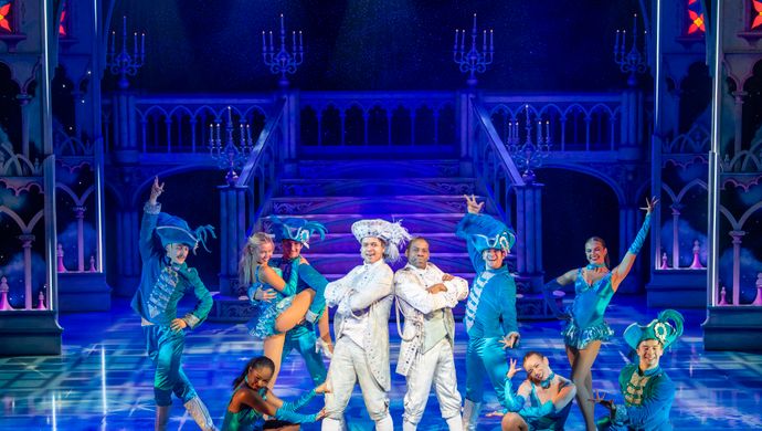 Prince charming and Dandini stand back to back dressed in white outfits with their arms folded.