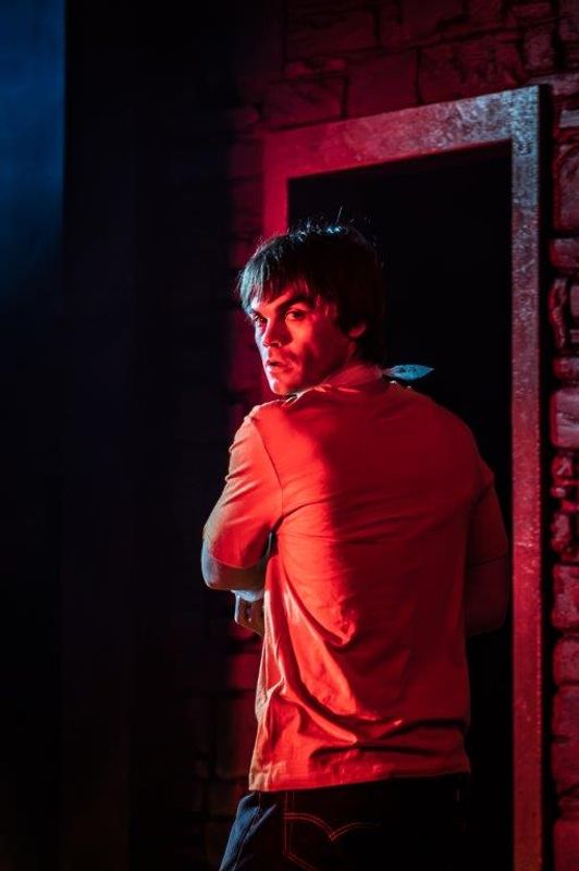 A man looks over his shoulder, he looks concerned, there is a red light shining on him