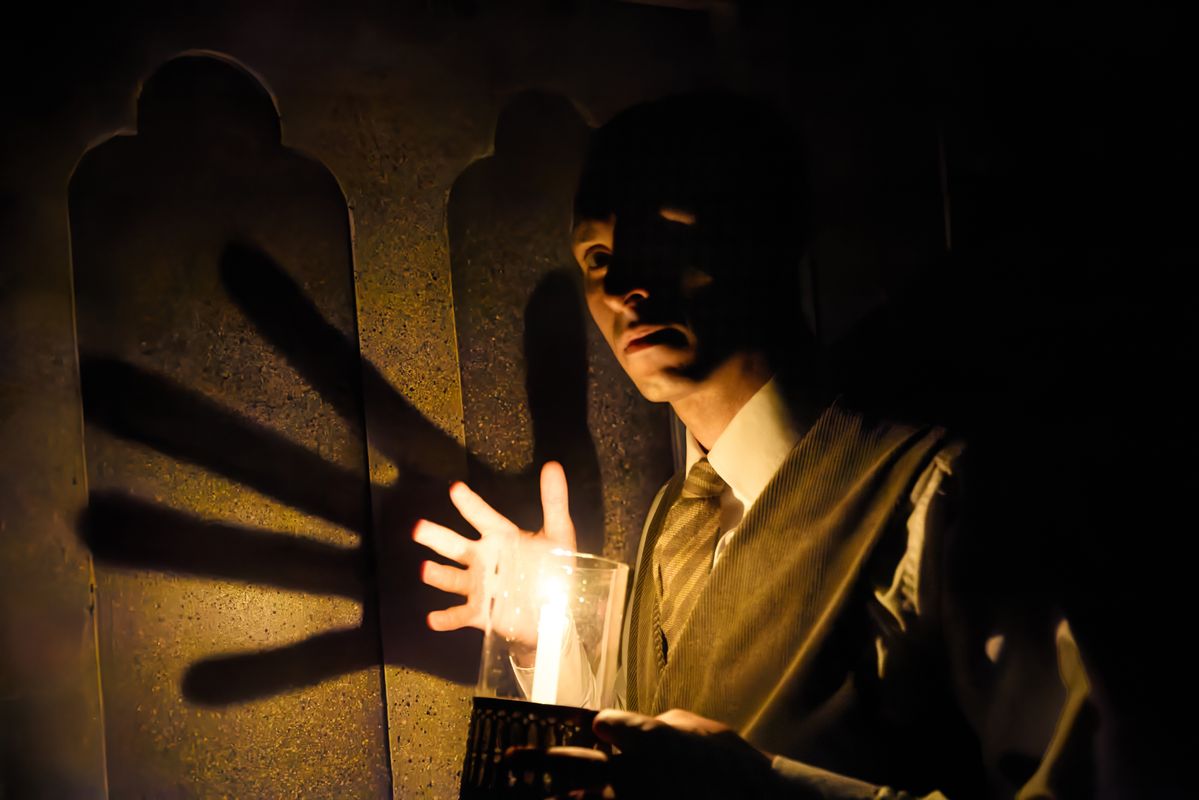 A person holds a candle with a shadow of their hand projected in the background.