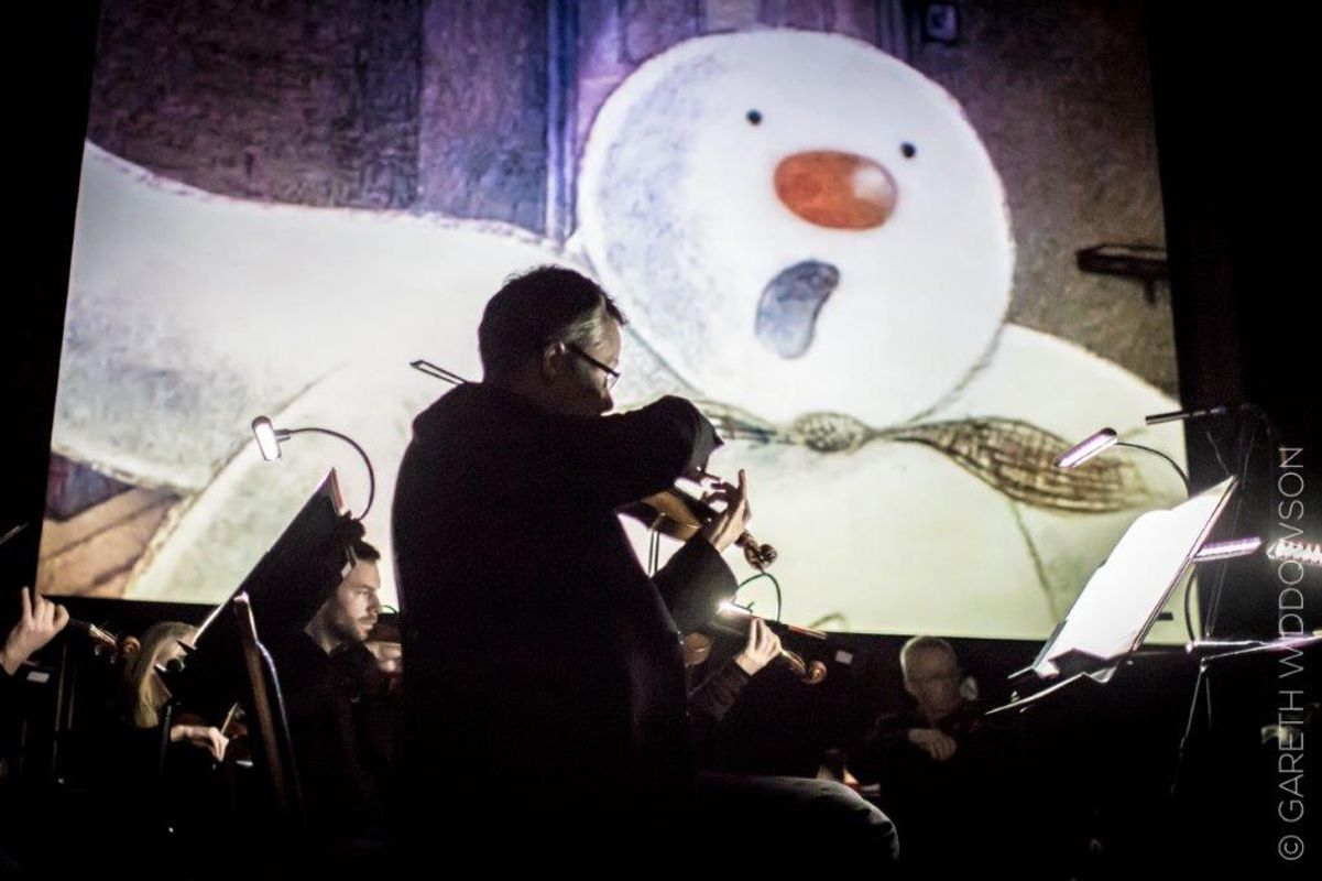 People performing on stage with The Snowman on a projector behind them.