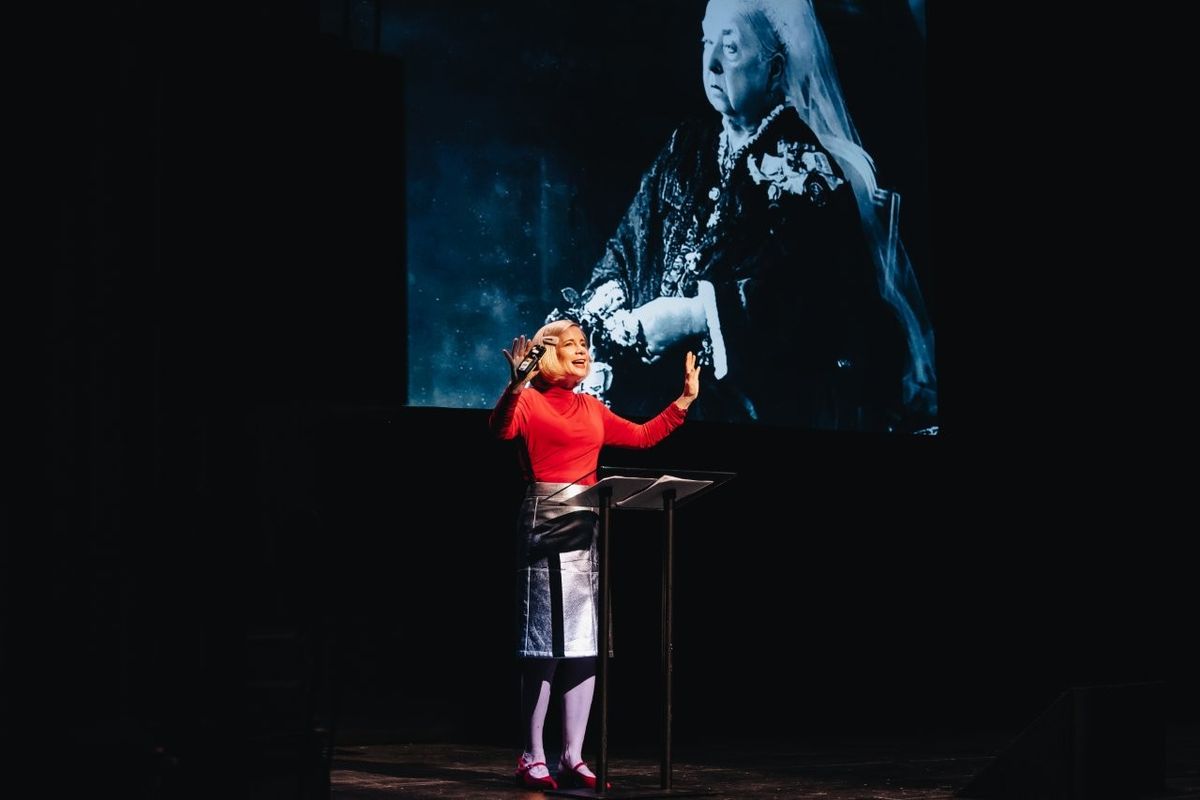 Lucy Worsley talking on stage. She is wearing a red top and a silver pencil skirt.
