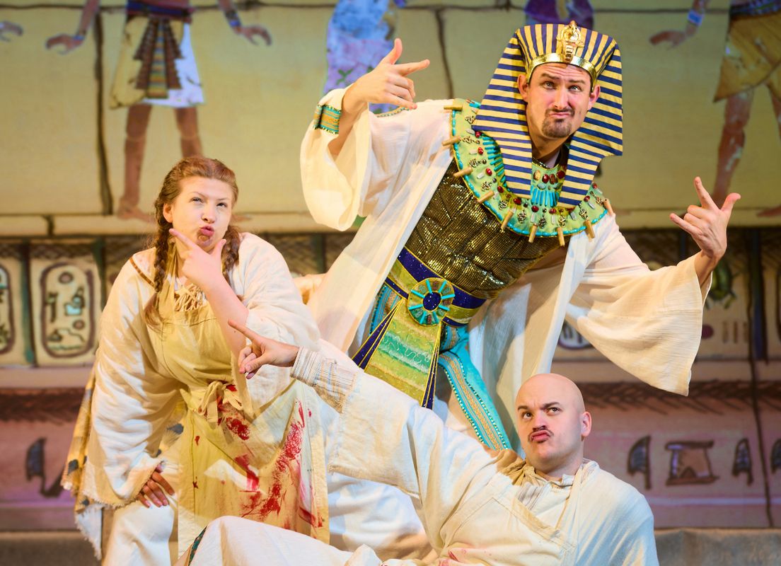 There are three people on stage, all in different poses. Two are dressed in ancient Egyptian clothing and the third is dressed as a pharaoh. 