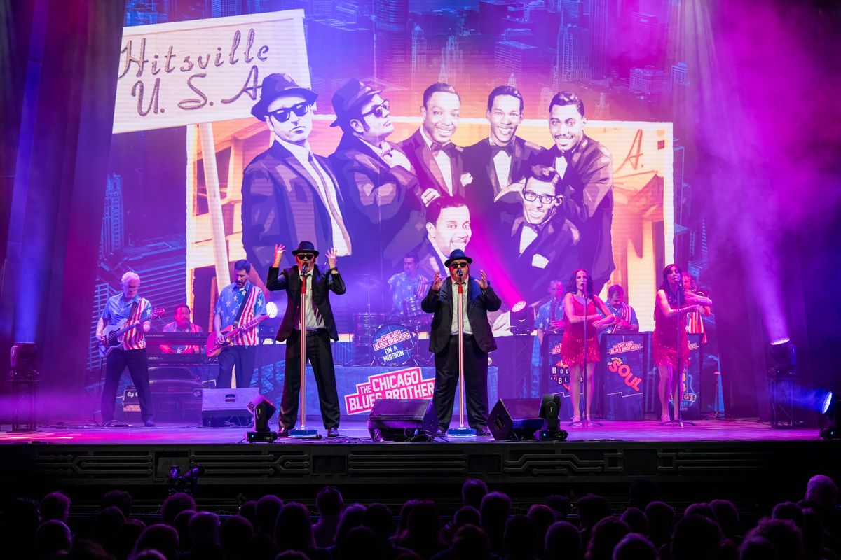 Two people dressed in black suits and bowler hats raise their arms in the air.