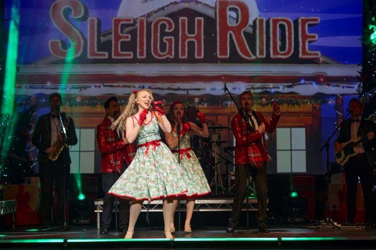 A person dressed in a 1950s style dress sings on stage.