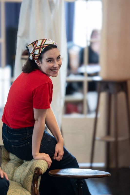 A woman in a red t-shirt and bandana is smiling over her shoulder