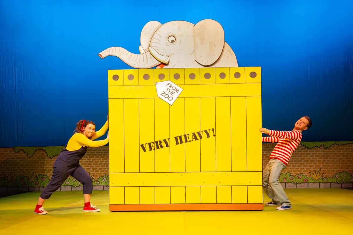 There is a giant yellow crate, with the words VERY HEAVY! on it, a cartoon elephant poking out the top.  Two people stood either side of the crate, one is trying to pull it and thoe other trying to push it.