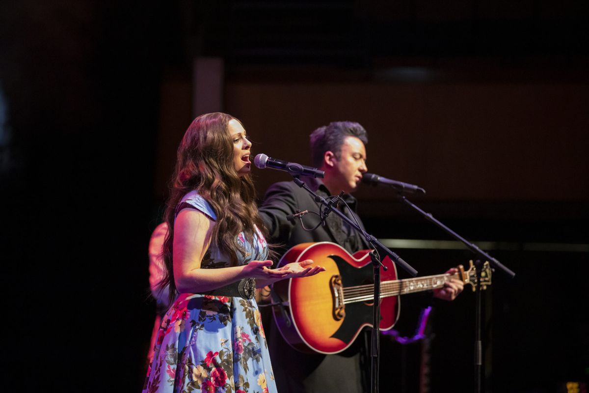 Two people stand on stage playing guitar and singing.