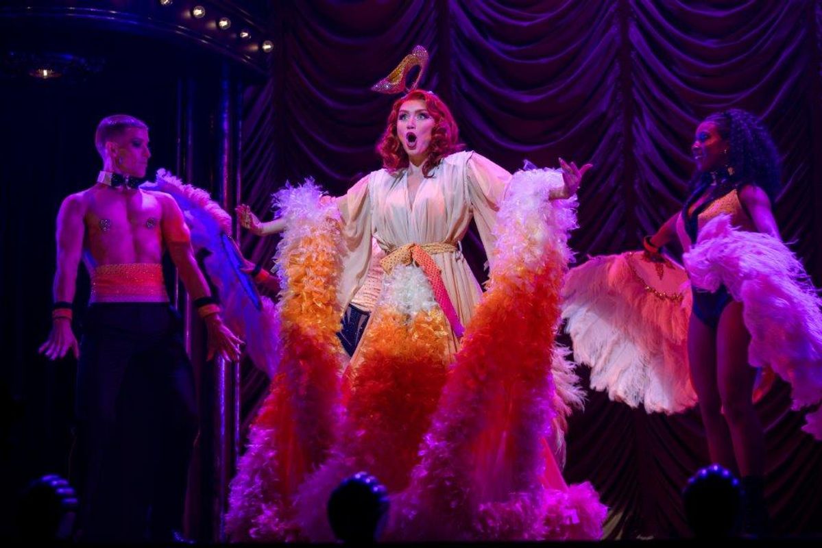 A performer wearing a dressing gown with feathers attached, there are two performers by her side