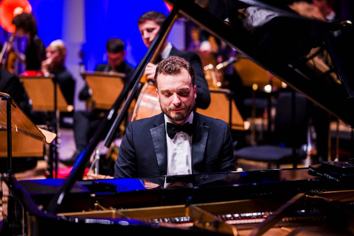 A musician wearing a white shirt and dickie bow plays the piano.
