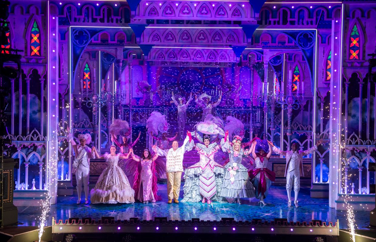 The Cinderella company stand centre stage with  their arms above their heads.