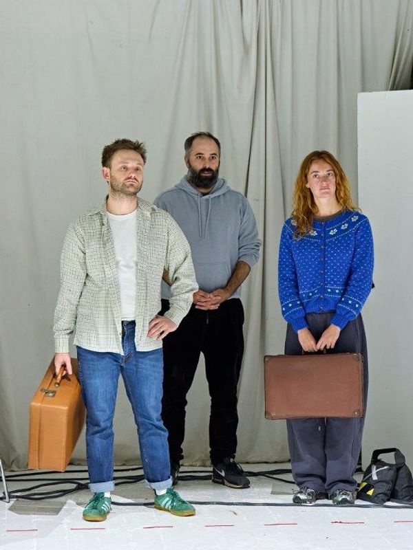 There are three people stood up, the two at the front are holding suitcases